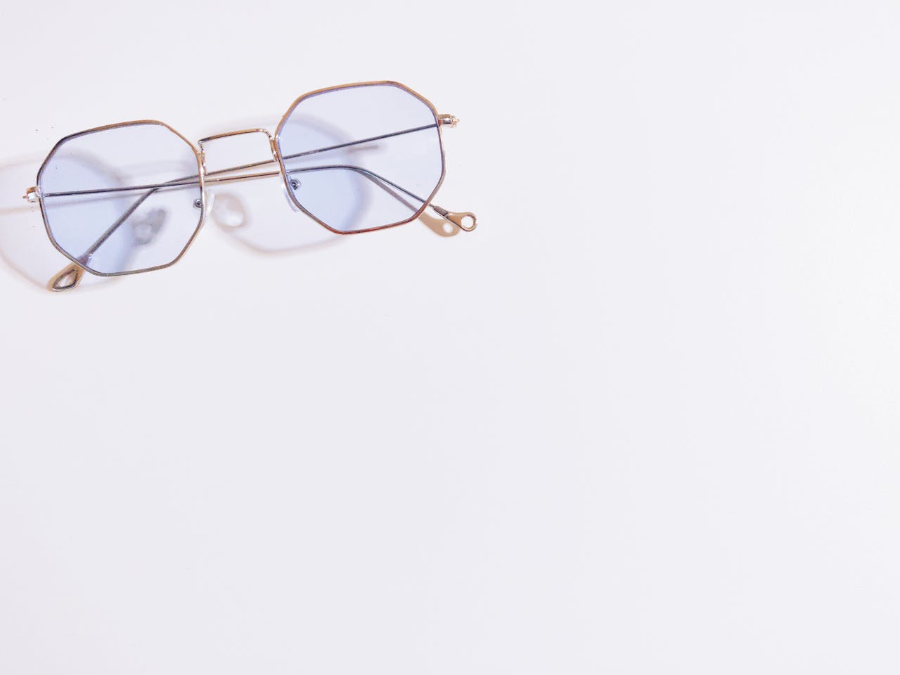 Close-up of hexagonal eyeglasses with blue tint on a white background, minimalistic style.